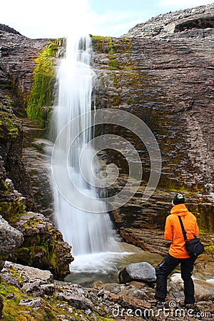 Girl standing near the beautiful waterfall and and looking at it