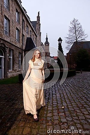 Girl in Victorian dress in a old city square in the evening walking