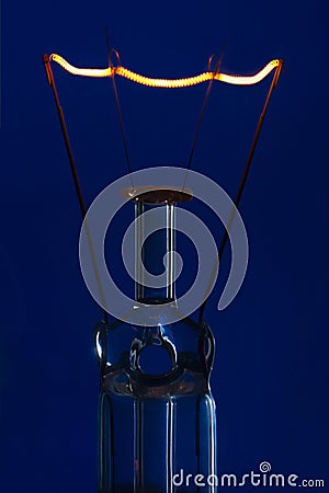 Glass light bulb with burning filament upright with blue backgro