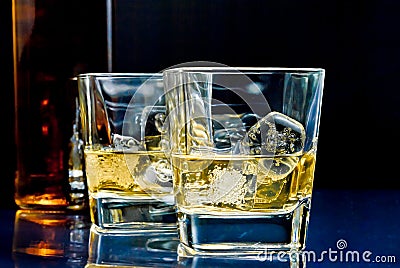 Glasses of alcoholic drink with ice on blue light