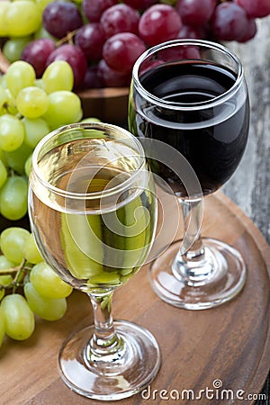 Glasses of white and red wine, fresh grapes on board