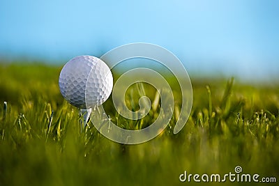 Golf ball sitting on tee with blue sky and grass b