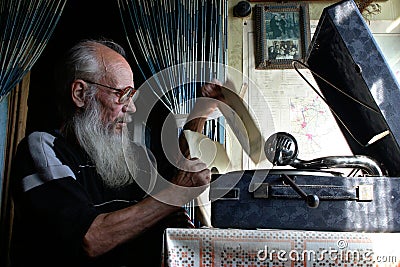 Graybeard old man in glasses sitting near an antique gramophone
