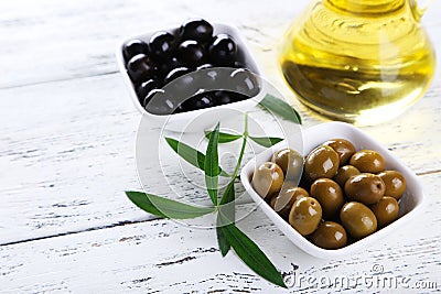 Green and black olives in bowl on white wooden background.