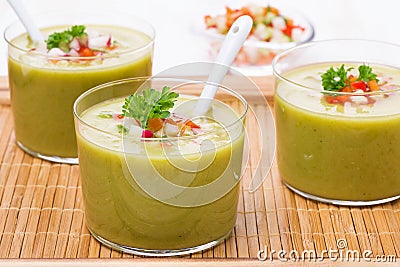 Green soup with fresh vegetables in glasses on wooden tray