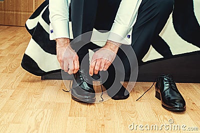 Groom wearing shoes on wedding day, tying the laces, preparing