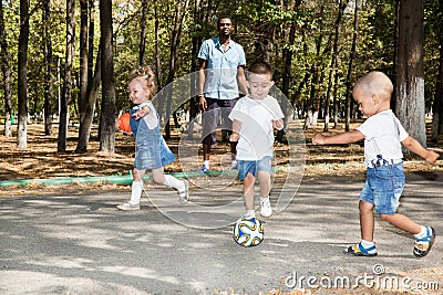 Group of happy children playing with soccer ball in park on nature at summer