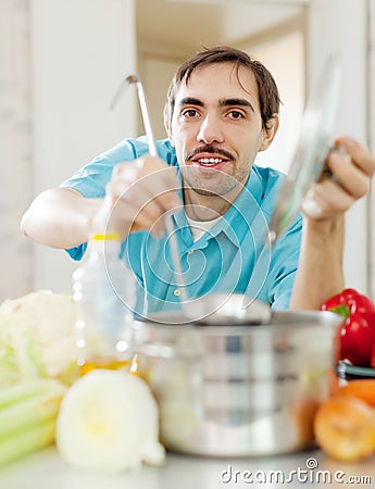 Guy with ladle cooking vegetables soup at kitchen
