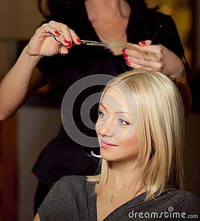 Haircutter cut hair in salon. Blonde woman