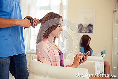 Hairdresser combing hair woman with mobile phone in hairdressing