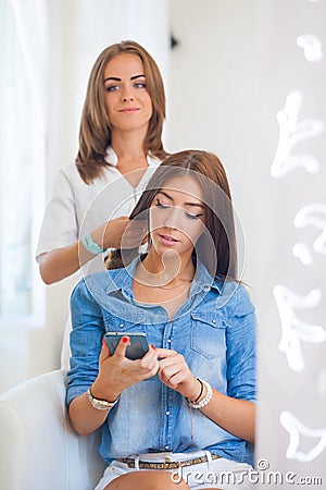 Hairdresser doing haircut for women wiht mobile phone in hairdre