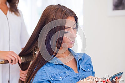 Hairdresser doing haircut for women wiht mobile phone in hairdre