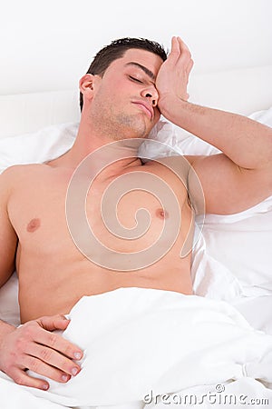 Half naked man waking up in the bedroom and stretches in bed