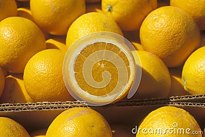 A halved orange rests on oranges in boxes