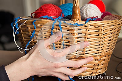Hand holding a basket with knitting needles and balls of wool
