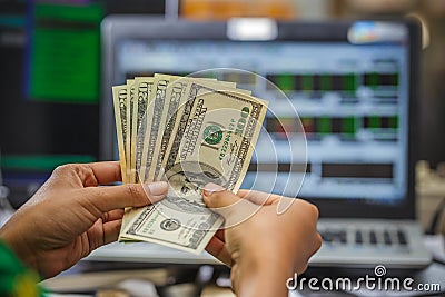 Hand holding money with display of stock market monitor on the background