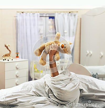 Hand holds toy bear above the bed