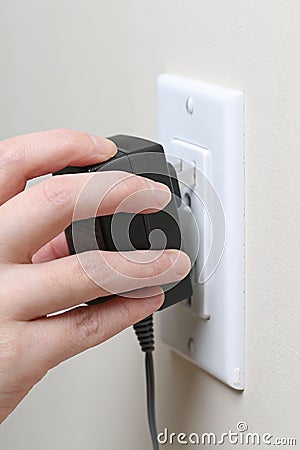 Hand inserting an electrical plug into a wall socket