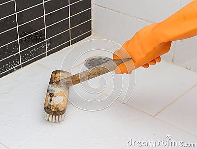 Hand in orange glove cleaning bathroom dirty floor