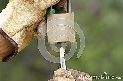 Hands in gloves with key and locked padlock