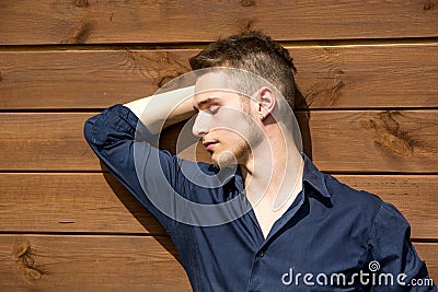 Handsome blond young man outside against wood wall