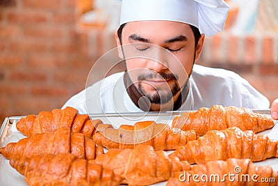 Cooking pastry. Cheerful young baker in apron smelling fresh baked croissants with closed eyes while standing on the background of a bakery shop. - handsome-cook-kitchen-cooking-pastry-cheerful-young-baker-apron-smelling-fresh-baked-croissants-closed-eyes-50487923