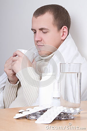 Handsome ill man drinking tea in living room. tablets in focus