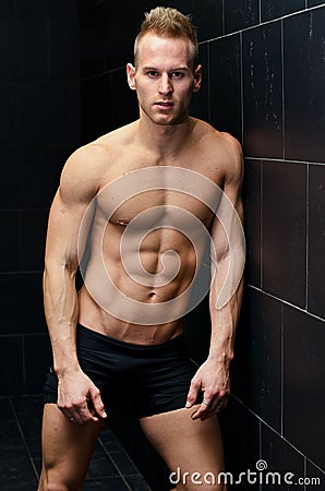 Handsome, muscular young man shirtless leaning against tiled wall