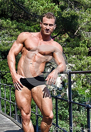 Handsome young bodybuilder shirtless outdoors in sunny day