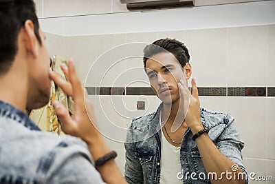 Handsome young man applying moisturizing cream on face
