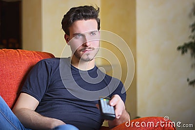 Handsome young man on counch, using TV remote control