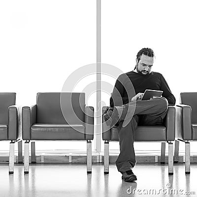 Handsome young man with dreadlocks using his digital tablet pc at an airport lounge, modern waiting room, with backlight