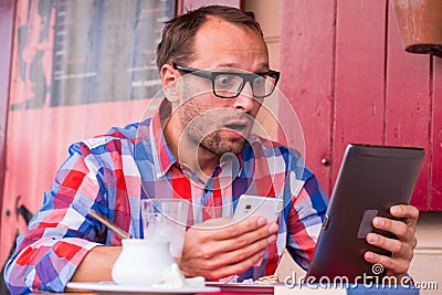 Handsome young man eating sandwich in restaurant. He is holding a phone and tablet.