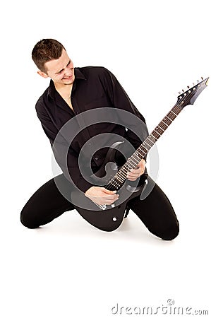 The handsome young man sits and plays the electric guitar
