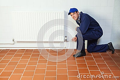 Handyman in blue boiler suit repairing a radiator smiling at camera