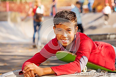 Happy Arabian boy in red shirt lays on skateboard