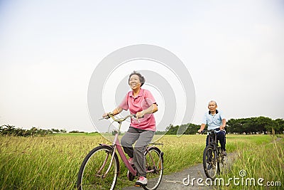 Happy Asian elderly seniors couple biking in the park with blue