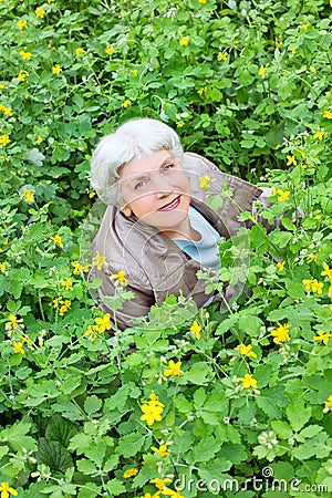 Happy beautiful elderly woman sitting on a glade
