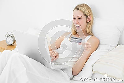 Happy blonde woman using her laptop for home shopping lying on h