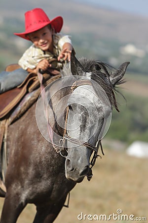 Happy boy in cowboy hat riding horse outdoors