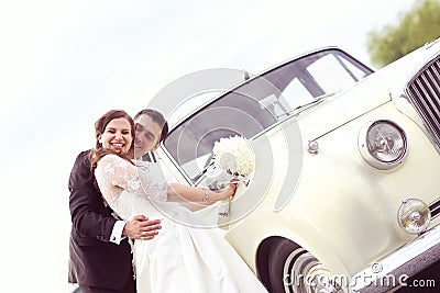 Happy bride and groom near retro car