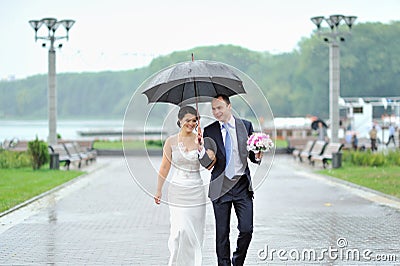 Happy bride and groom walking by the rain on their wedding day