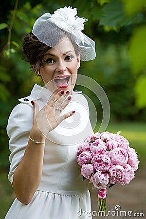 Happy bride laughing, covering mouth with her hand with bouquet of peony flowers.