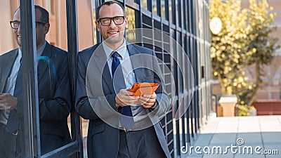 Happy business man using tablet PC in orange cover on a city str