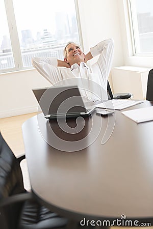 Happy Businessman With Hands Behind Head Sitting At Desk