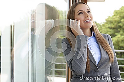 Happy businesswoman answering cell phone by glass door