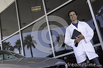 Happy car dealer standing in front of car showroom