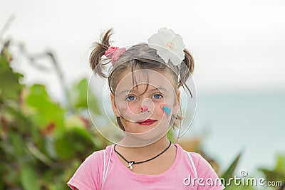 Happy child girl with surprised reaction on her painted face standing near the beach against the ocean and tropical garden backgro