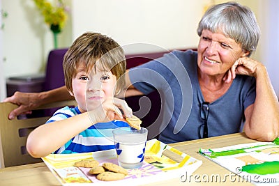 Happy child having snack during homework with smiling grandma