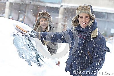 Happy couple brushing off snow from car
